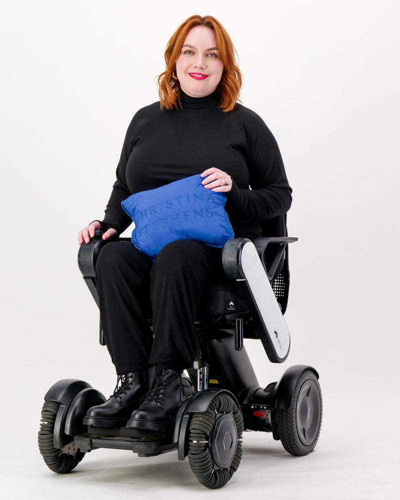 Our seated model with red hair and who is in a wheelchair is wearing a black thermal top with long sleeves, black pants and black boots. Christina Stephens Adaptive Clothing Australia.