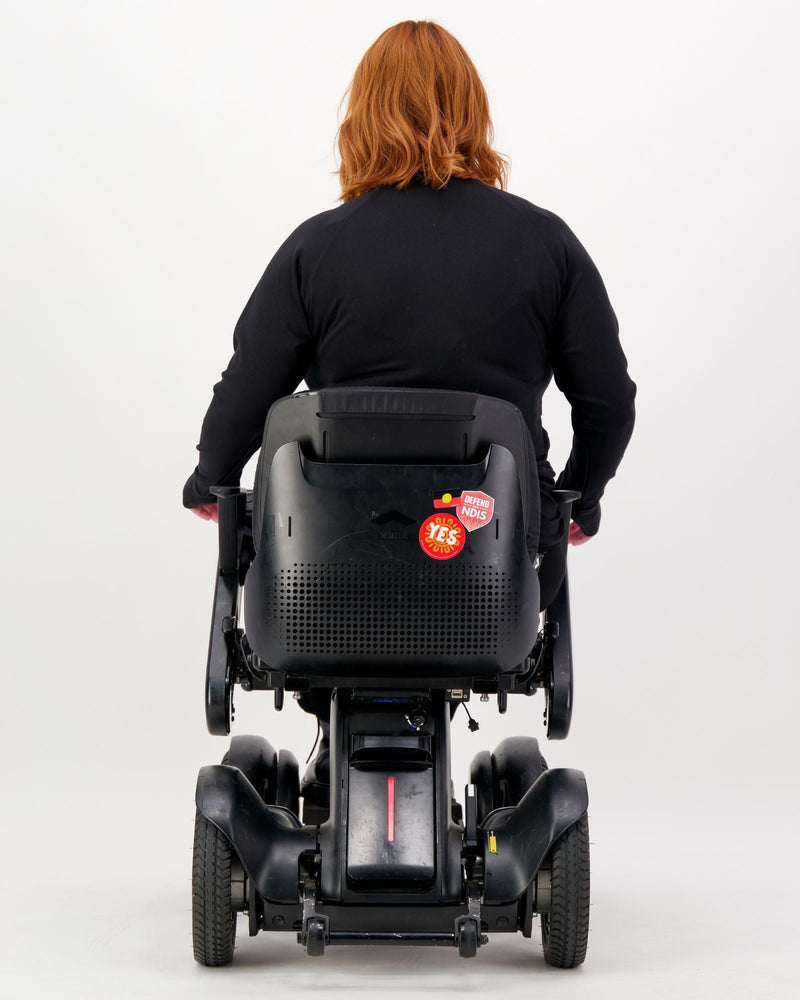 Our seated model with red hair and who is in a wheelchair is wearing a black thermal top with long sleeves, black pants and black boots. Christina Stephens Adaptive Clothing Australia.