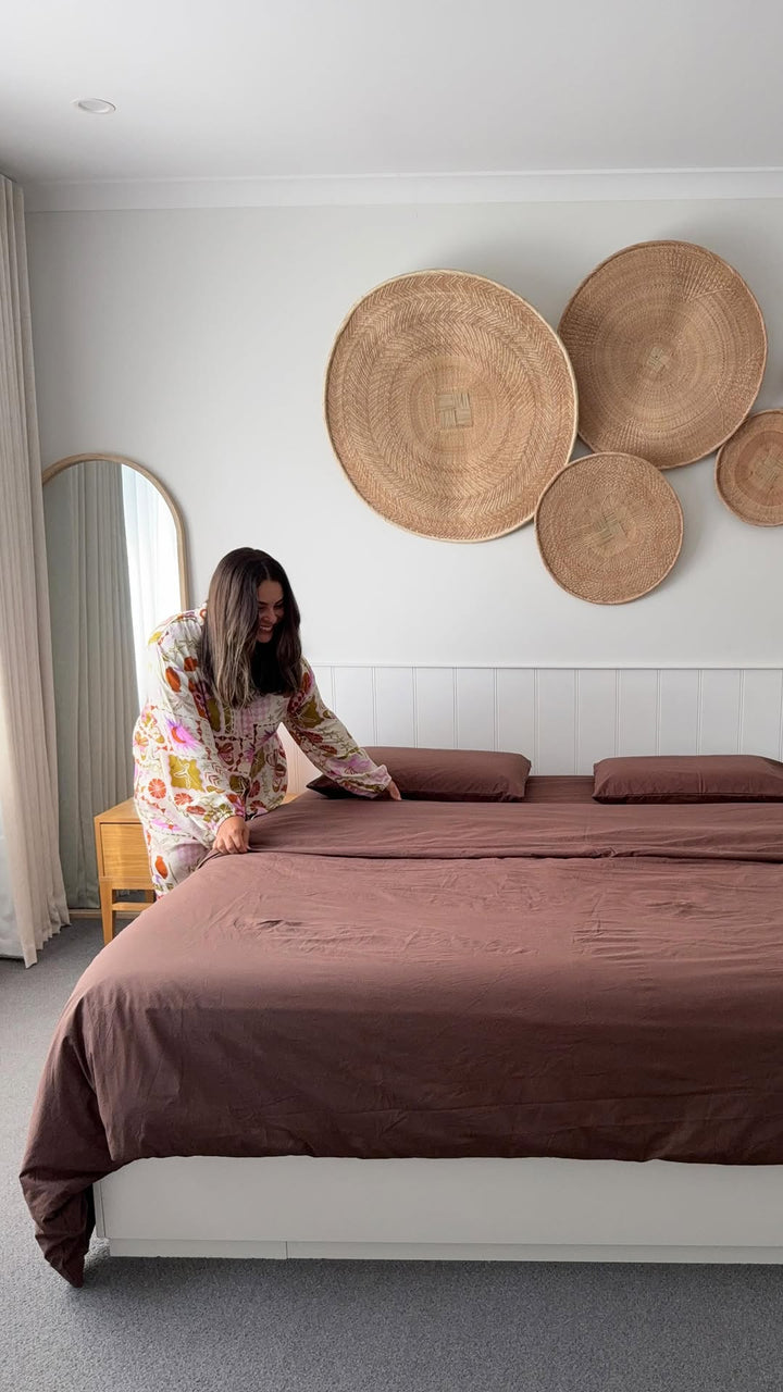 Woman arranging bedding in a bedroom with decorative wall plates.