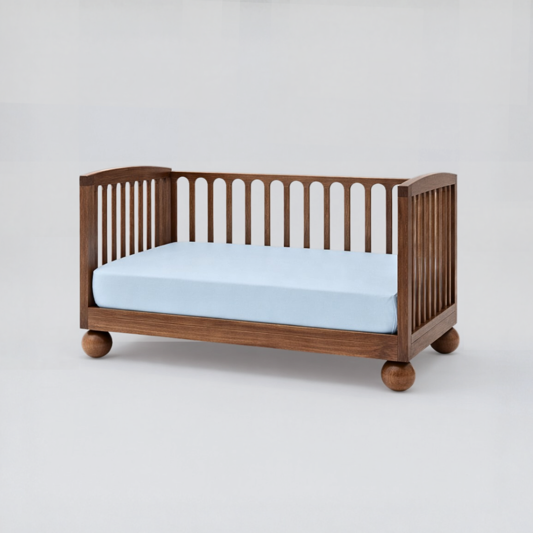 Wooden crib with a light blue mattress on a white background