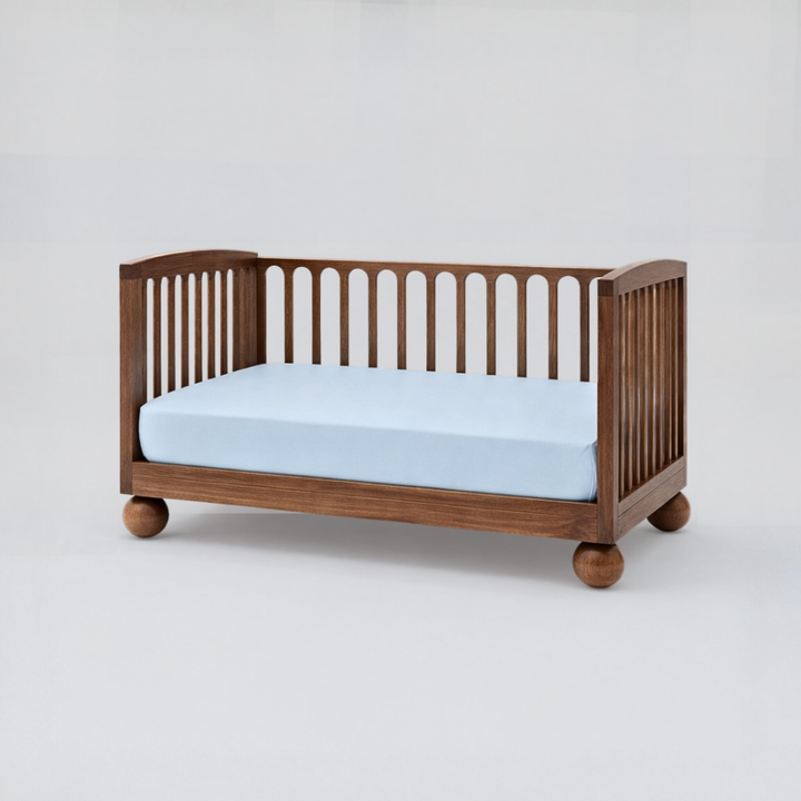 Wooden crib with a light blue mattress on a white background