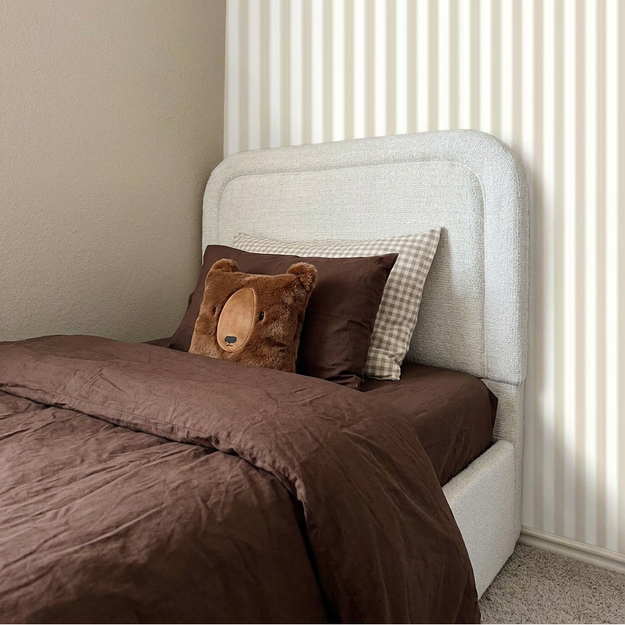 Bed with brown bedding and a teddy bear pillow against a white headboard.