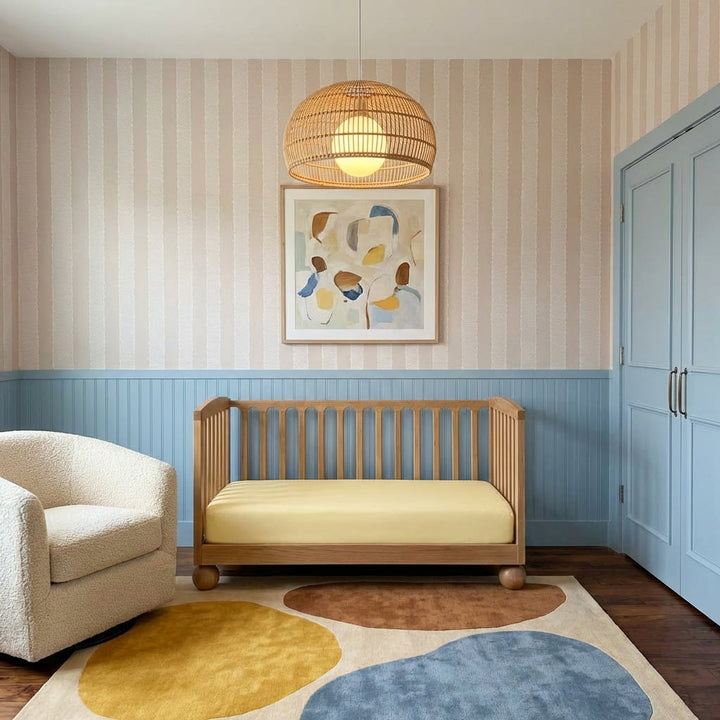 Nursery room with wooden crib, armchair, and abstract art on striped wall.