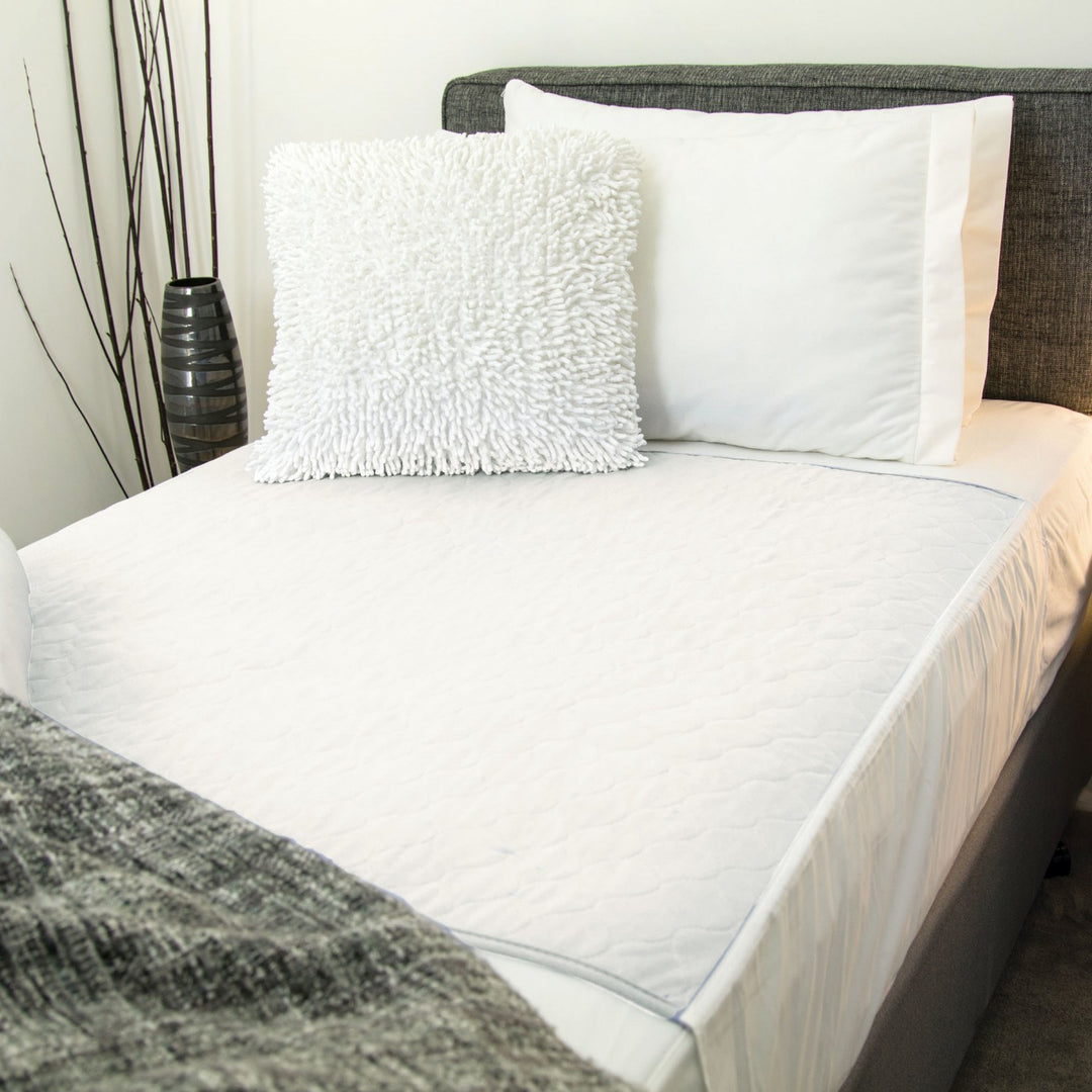 White Conni bed pad with tuck-ins, made of Manchester fabric, designed for secure, comfortable bedding protection.