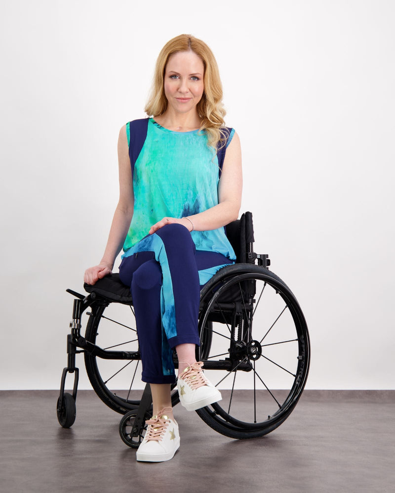 Blonde female sitting in a manual wheelchair wearing an aqua blue printed and navy sleeveless top. Christina Stephens Adaptive Clothing Australia.