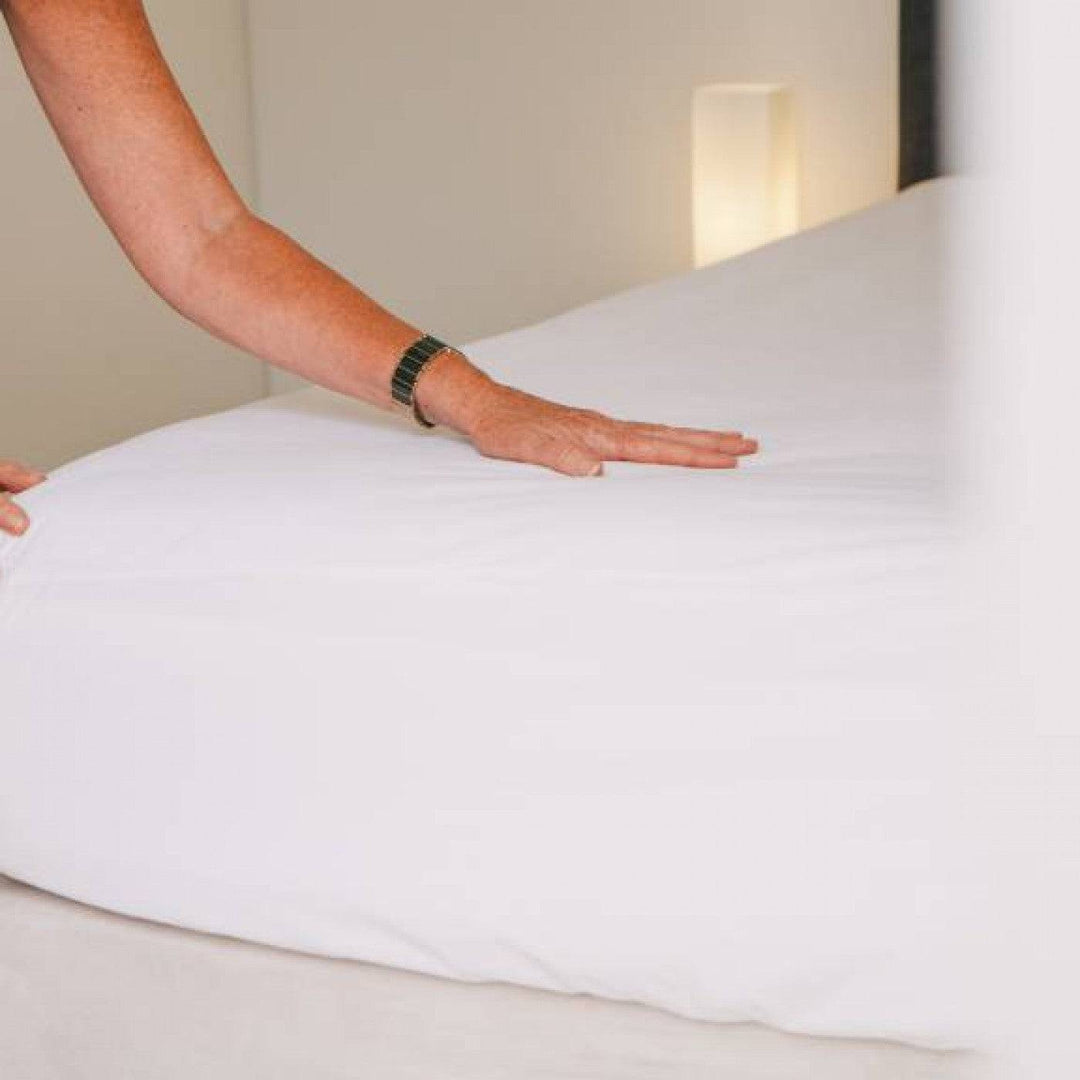 Conni Micro-Plush waterproof fitted sheet on a bed, soft Manchester fabric, with elastic edges for a snug fit.