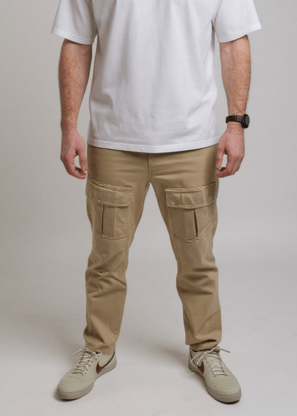 A man visible from the chest down wearing a white t-shirt and sand colour cargo pants on a plain background