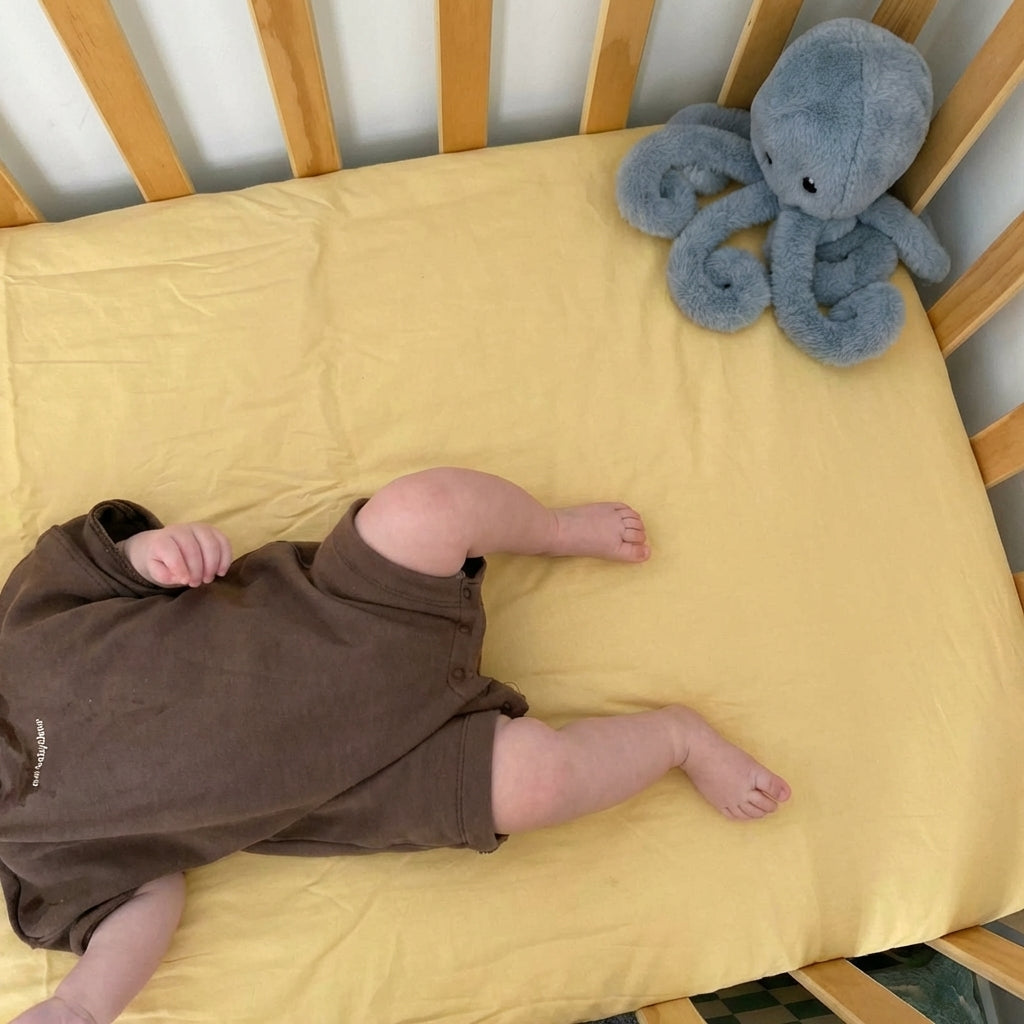 Baby lying on a yellow blanket in a crib with a plush toy next to them
