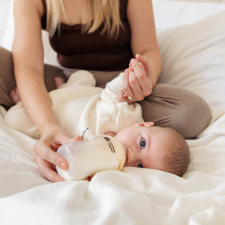 Woman holding a baby bottle with a baby on a bed