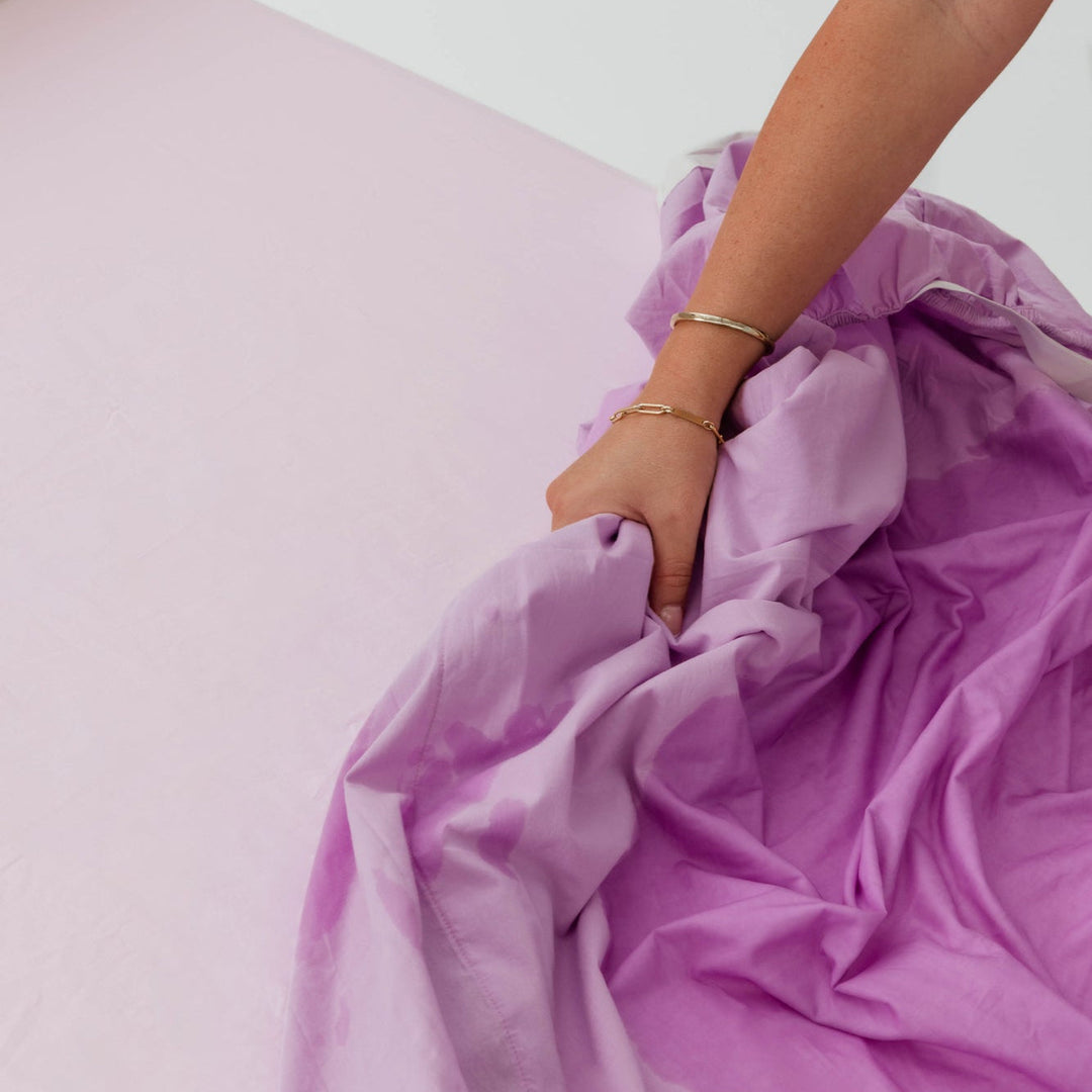 Person holding a purple blanket over a bed with a white background