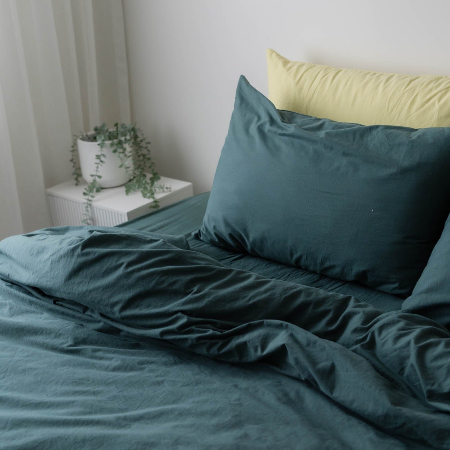 Teal bedding set with a yellow pillow on a bed in a room.