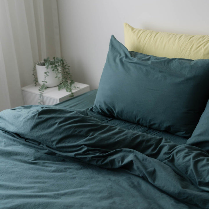 Teal bedding set with a yellow pillow on a bed in a room.