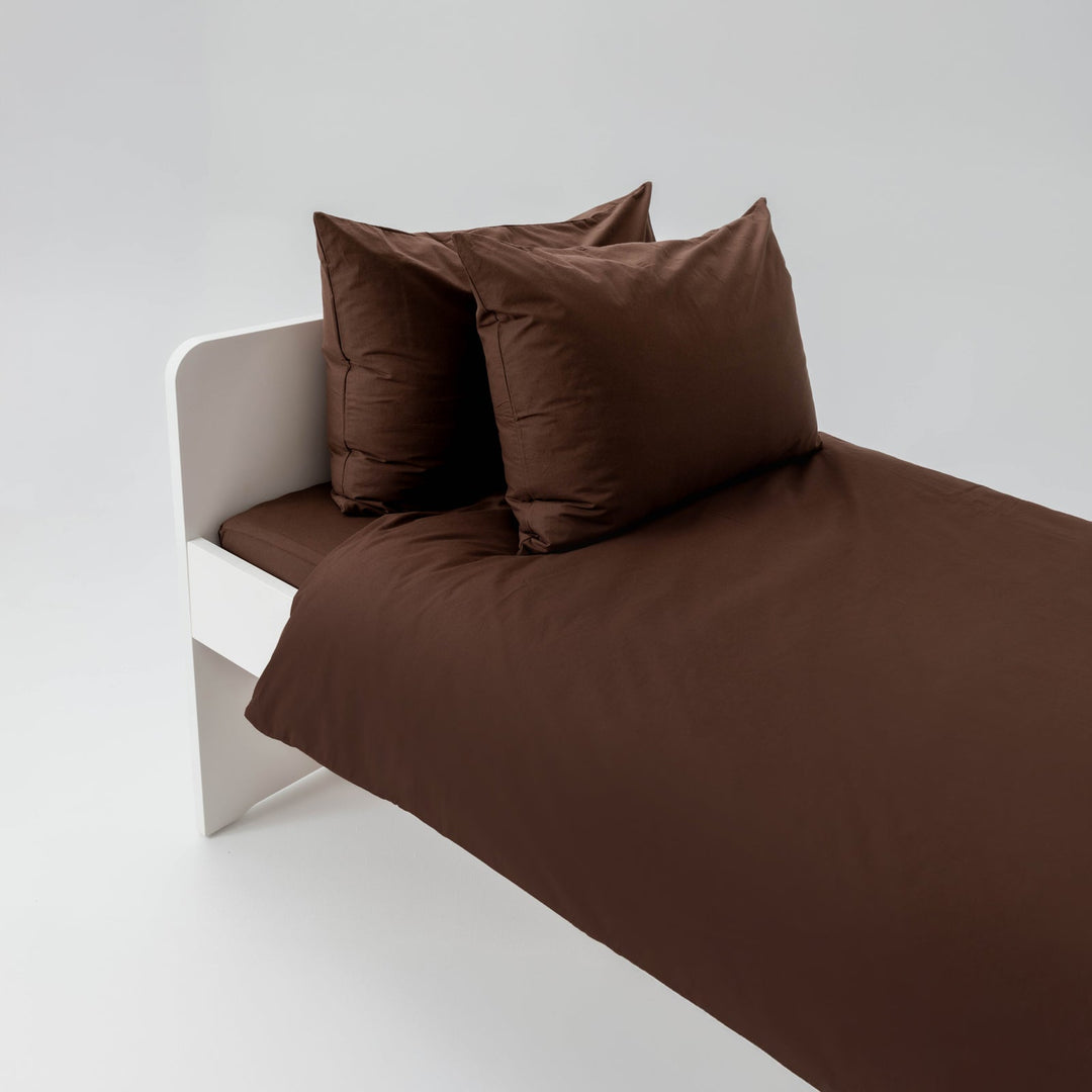 Brown bed sheets and pillows on a white bed frame against a light gray background
