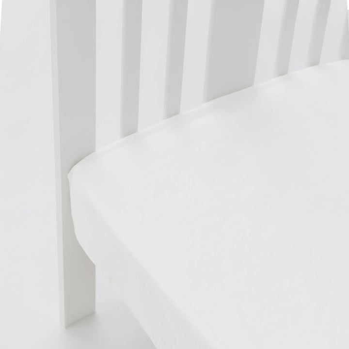 White crib with a fitted sheet on a white background