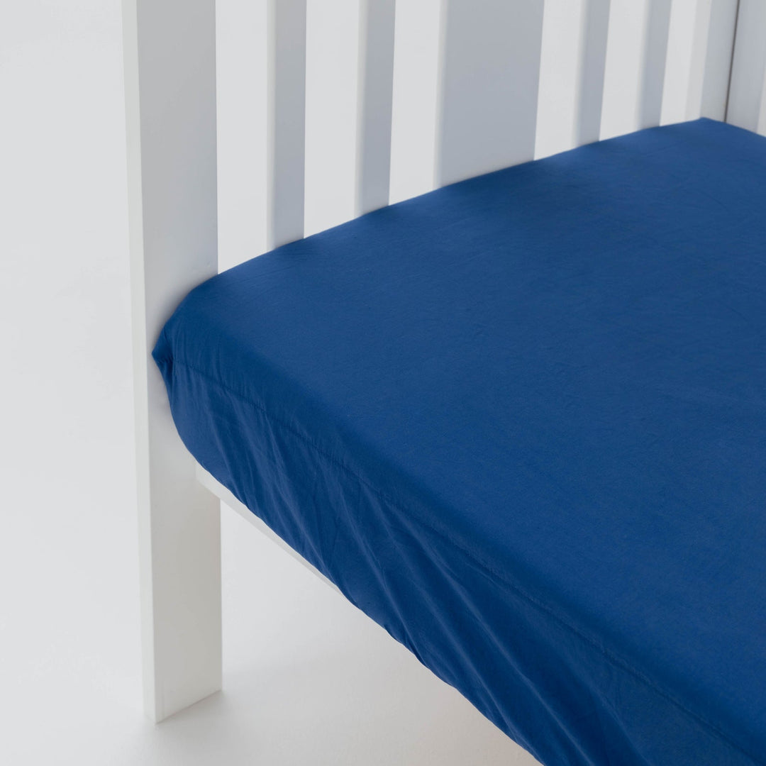 Blue fitted sheet on a white crib with white walls in the background