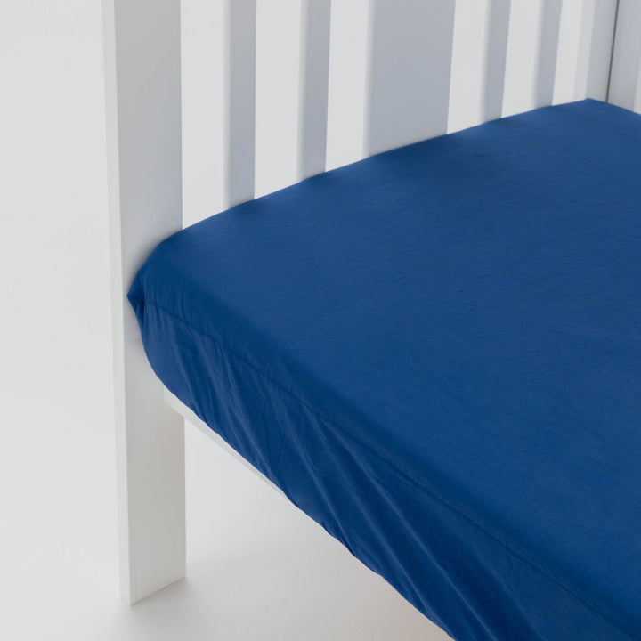 Blue fitted sheet on a white crib with white walls in the background
