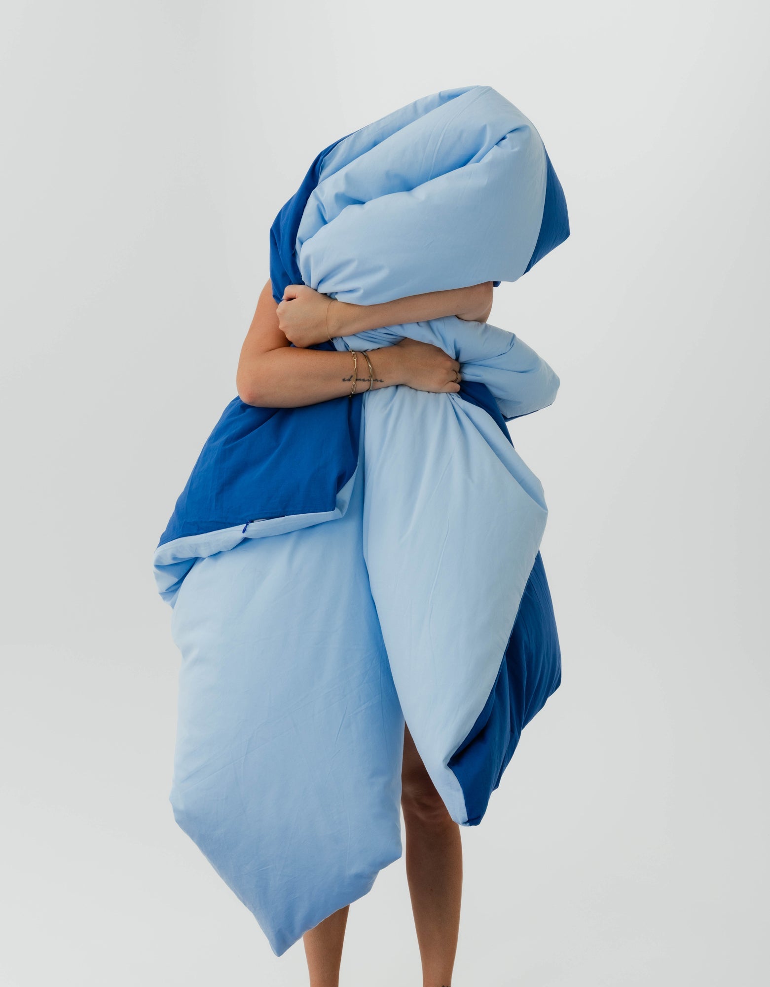 Person wrapped in a blue blanket against a light gray background