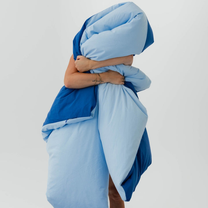 Person wrapped in a blue blanket on a plain background
