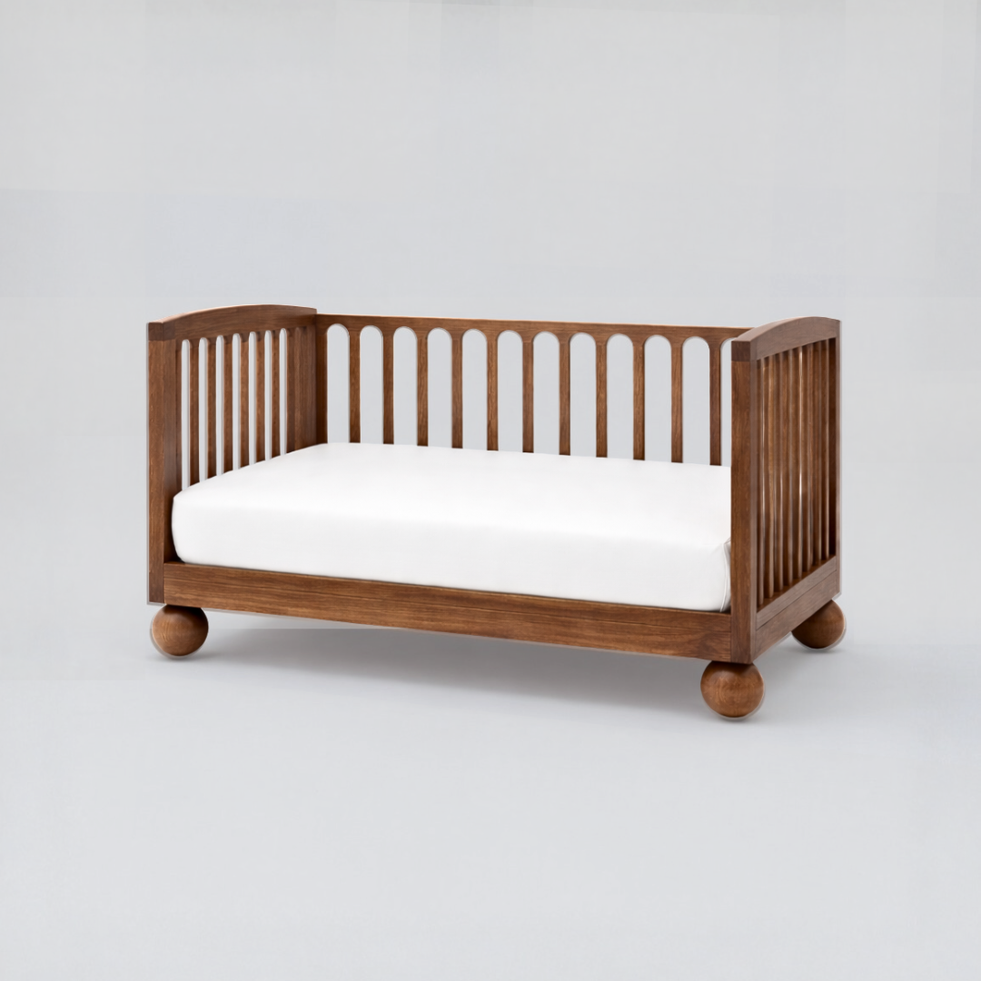 Wooden crib with a white mattress on a light gray background
