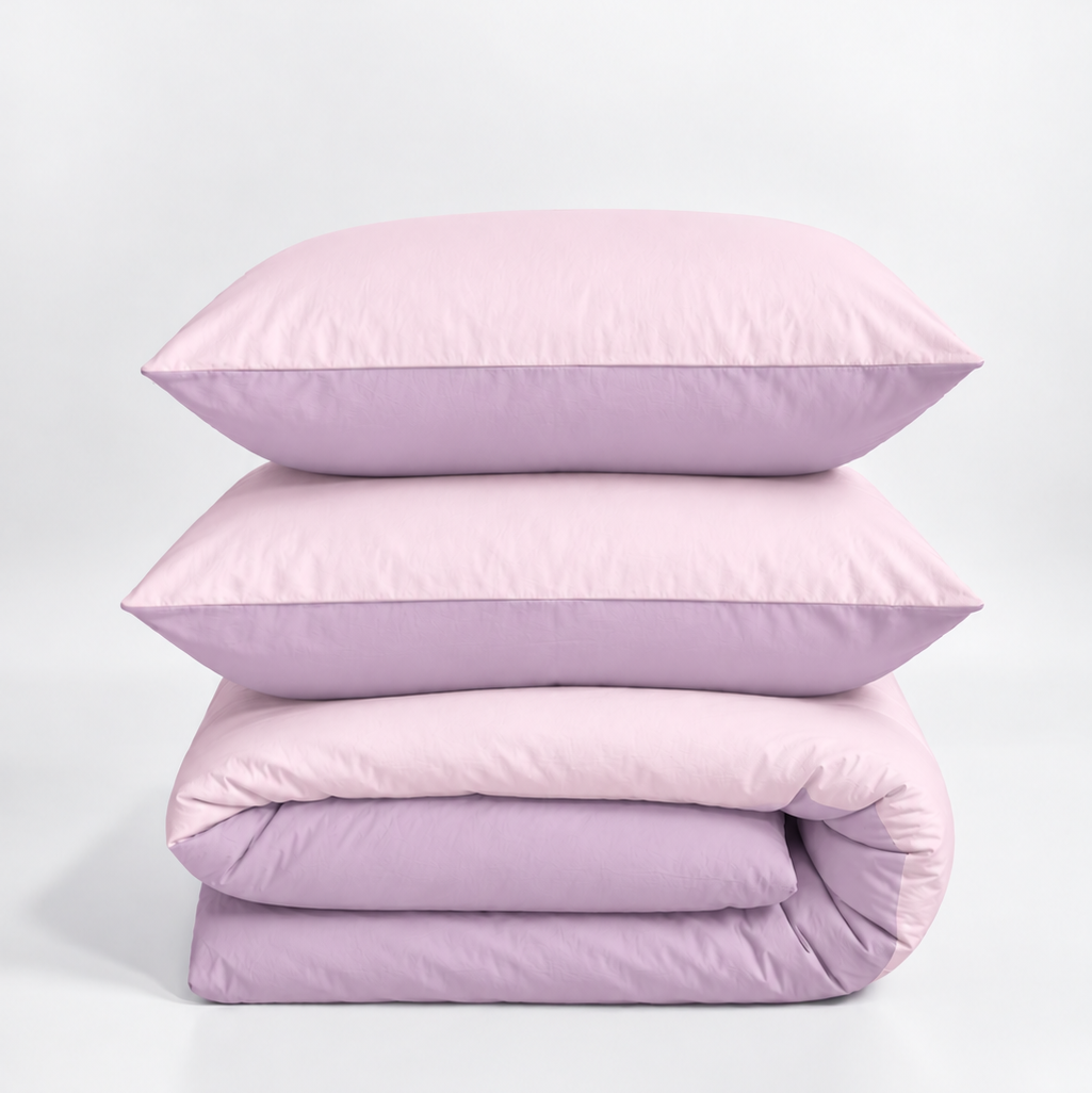 A stack of three light purple bedding items, including two pillows and a folded duvet cover, photographed on a clean white studio background.