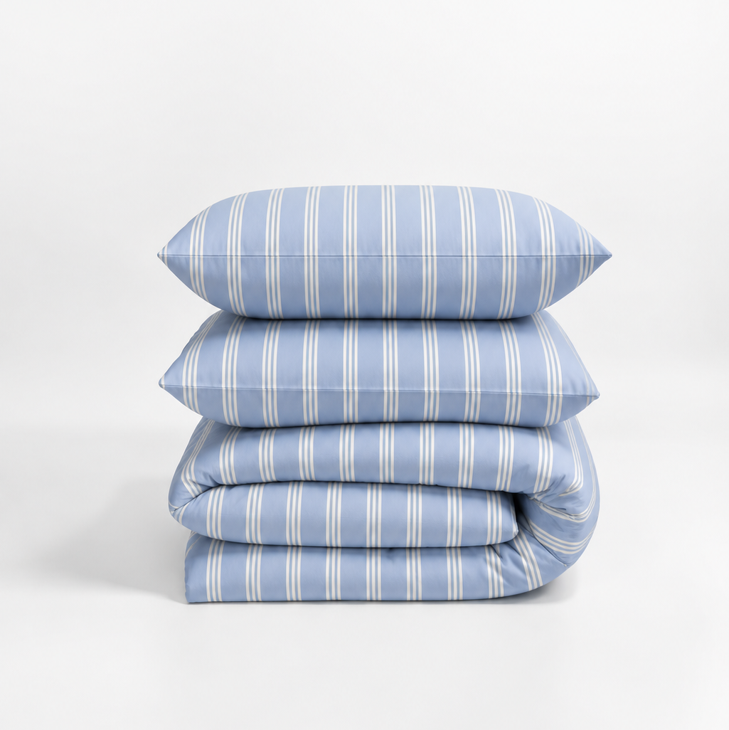 A stack of four light blue bedding items with thin white vertical stripes, including two pillows and two folded sheets, photographed on a clean white studio background.
