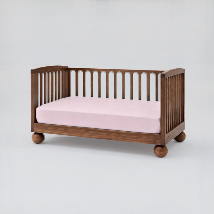 Wooden crib with pink mattress on a white background