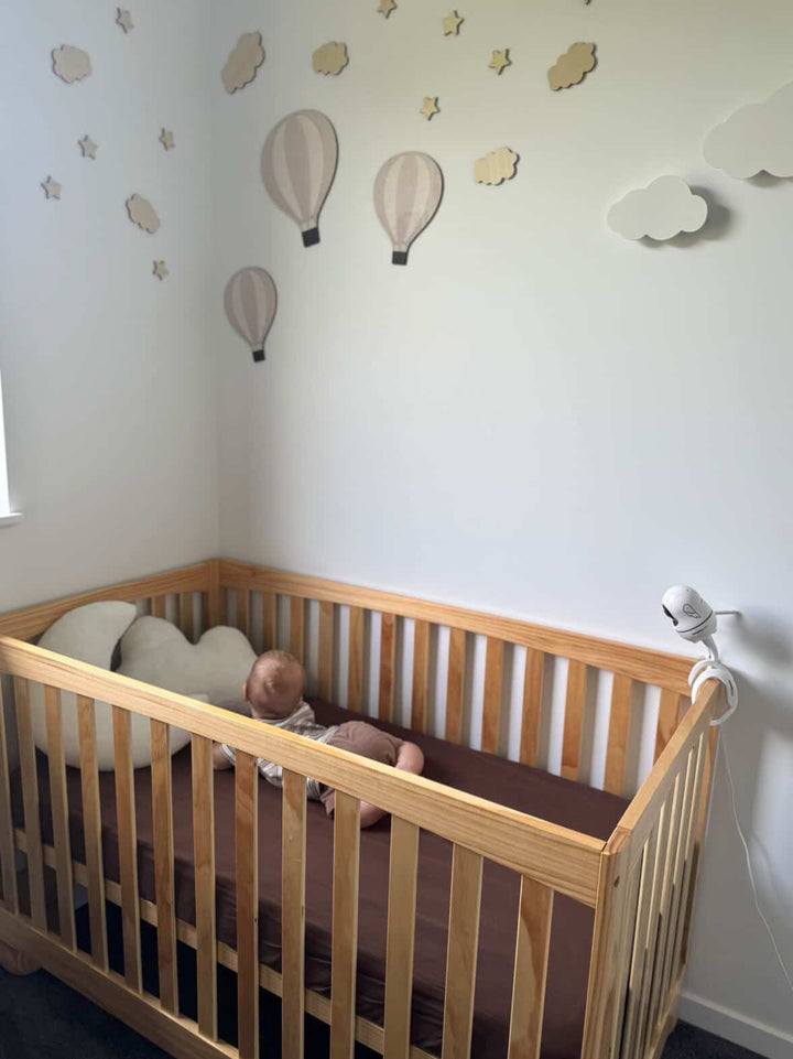 Baby in a wooden crib with decorative hot air balloons on the wall