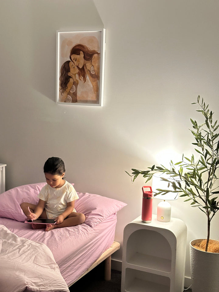 Person sitting on a bed in a bedroom with a painting on the wall and a plant.