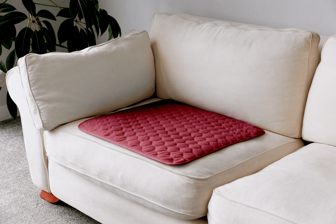 A red quilted cushion pad with a diamond pattern resting on a cream-colored fabric sofa in a living room setting.