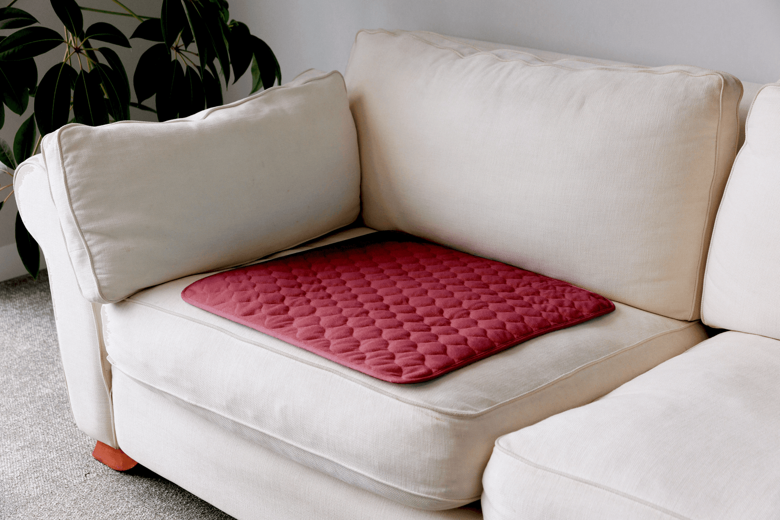 A red quilted cushion pad with a diamond pattern resting on a cream-colored fabric sofa in a living room setting.
