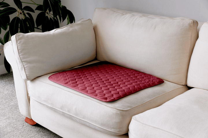 A red quilted cushion pad with a diamond pattern resting on a cream-colored fabric sofa in a living room setting.
