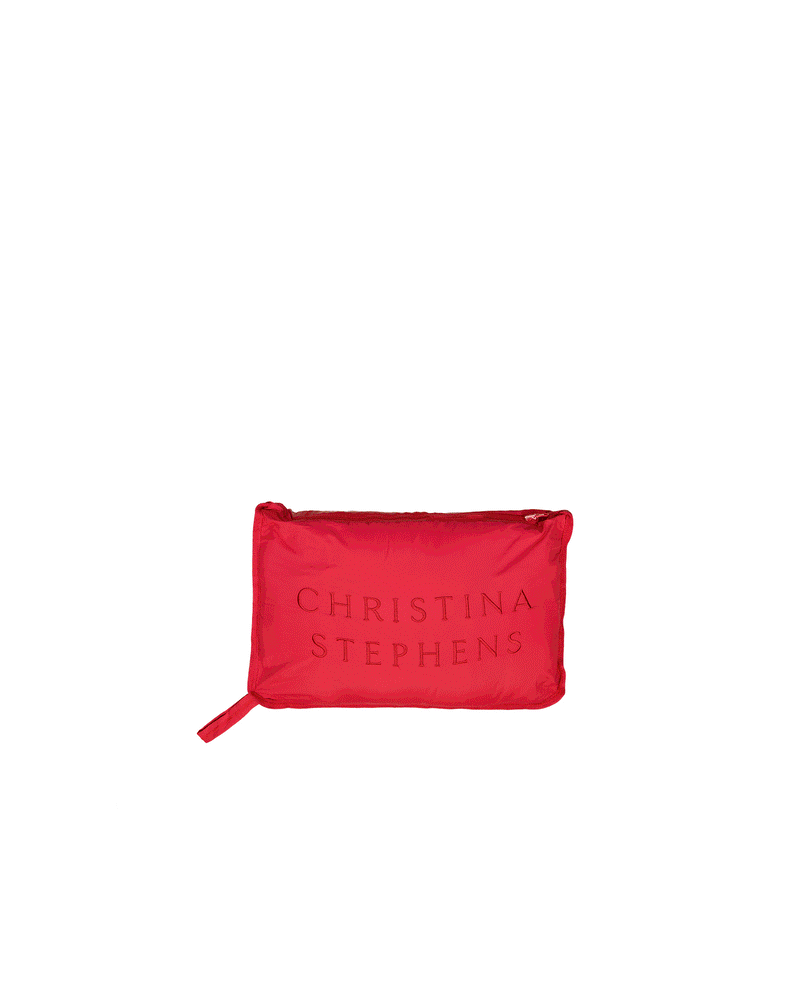 Elly Universal Puffer Jacket shown folded into its compact travel pillow form, displaying a vibrant red color with embossed text on the surface. The rectangular pillow features clean lines and a zip closure, demonstrating the jacket&