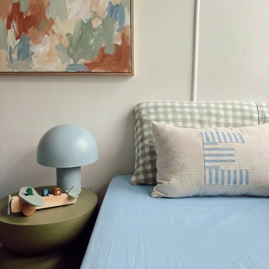 Bedroom with a lamp on a nightstand, colorful pillows, and abstract art on the wall.