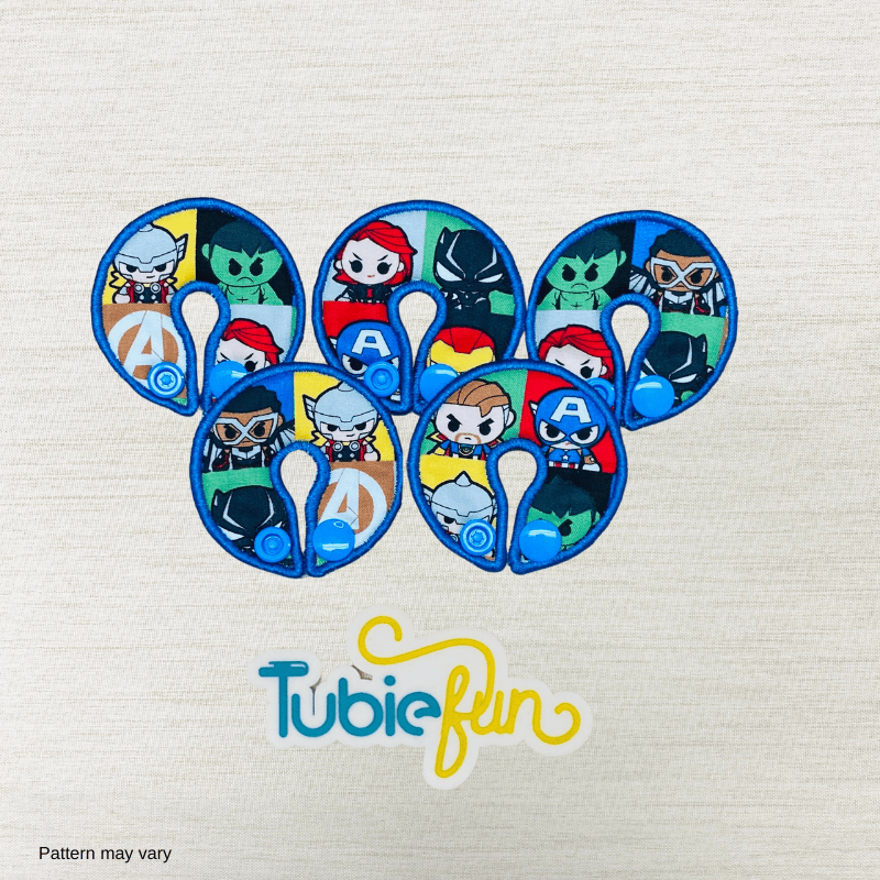 Five colorful superhero G-tube button pads by Tubie Fun, designed for nutrition support and comfort.