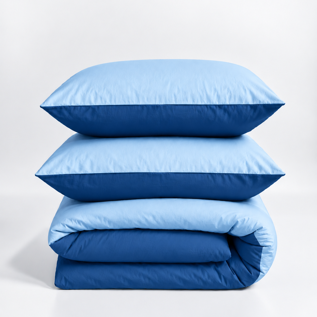 A stack of bedding set including two light blue pillows and a matching light blue and dark blue folded duvet on a white studio background.