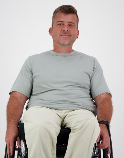 Man with light brown, short hair, is in a khaki t-shirt and cream cargo pants. Christina Stephens Australian Adaptive Clothing. 