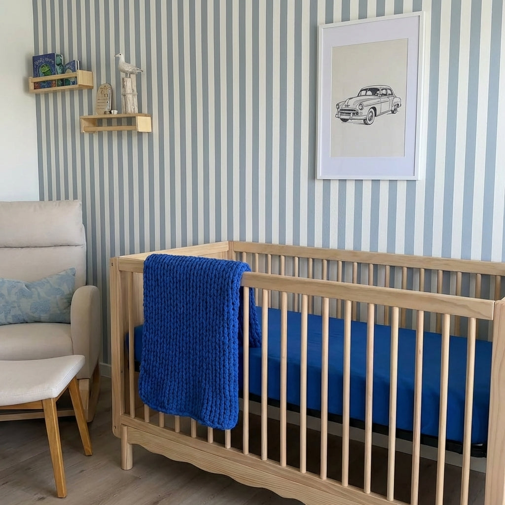 Nursery room with wooden crib, blue blanket, and striped wallpaper.
