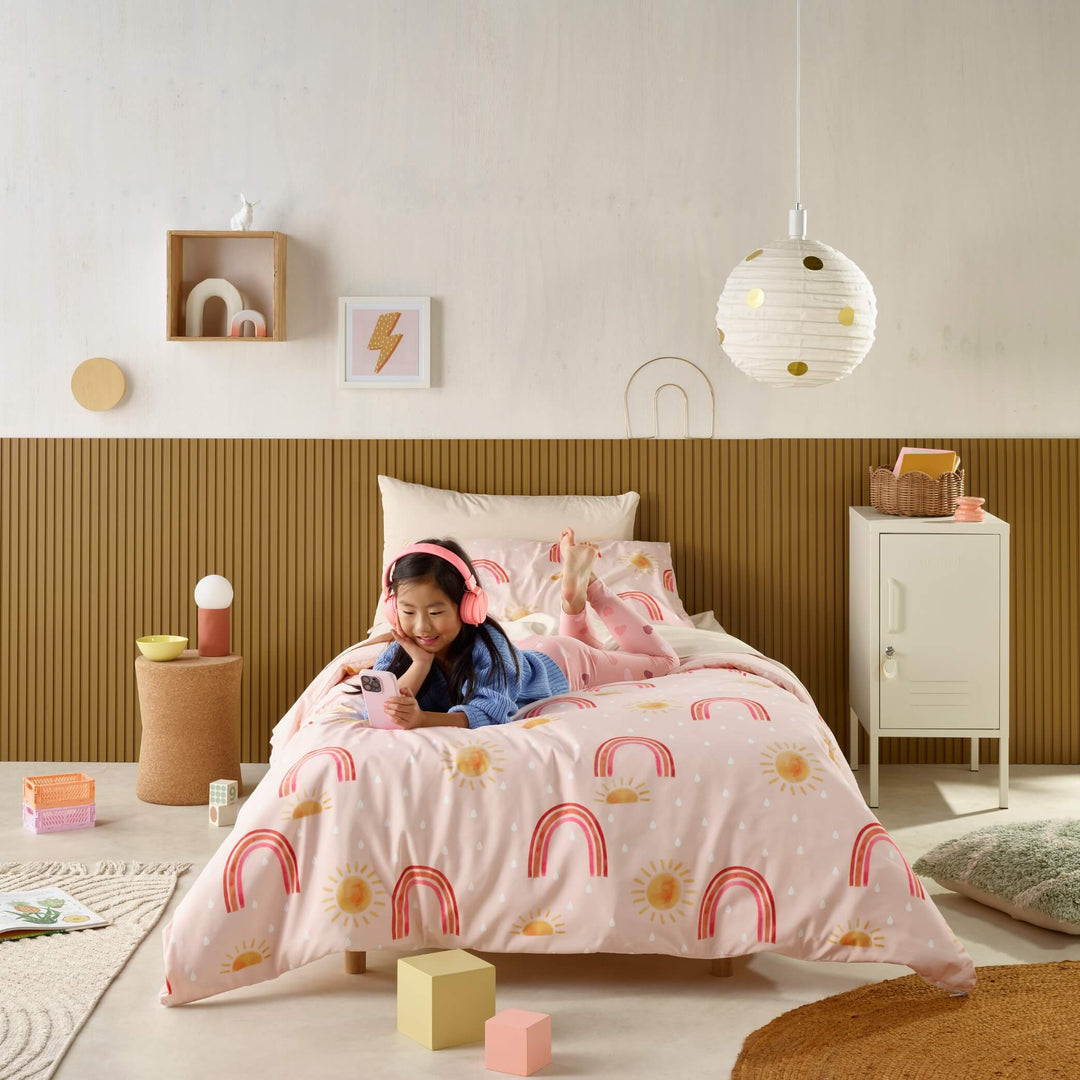 Girl using phone on bed with pink rainbow waterproof bedding and sheets for toilet training.