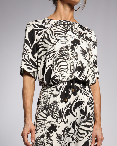 Lilli Leaf Back T-Shirt featuring bold black and white tropical print pattern on luxurious bamboo fabric, with relaxed fit design and three-quarter length sleeves. Side view showcases artistic leaf motif and belted waist detail against grey background.