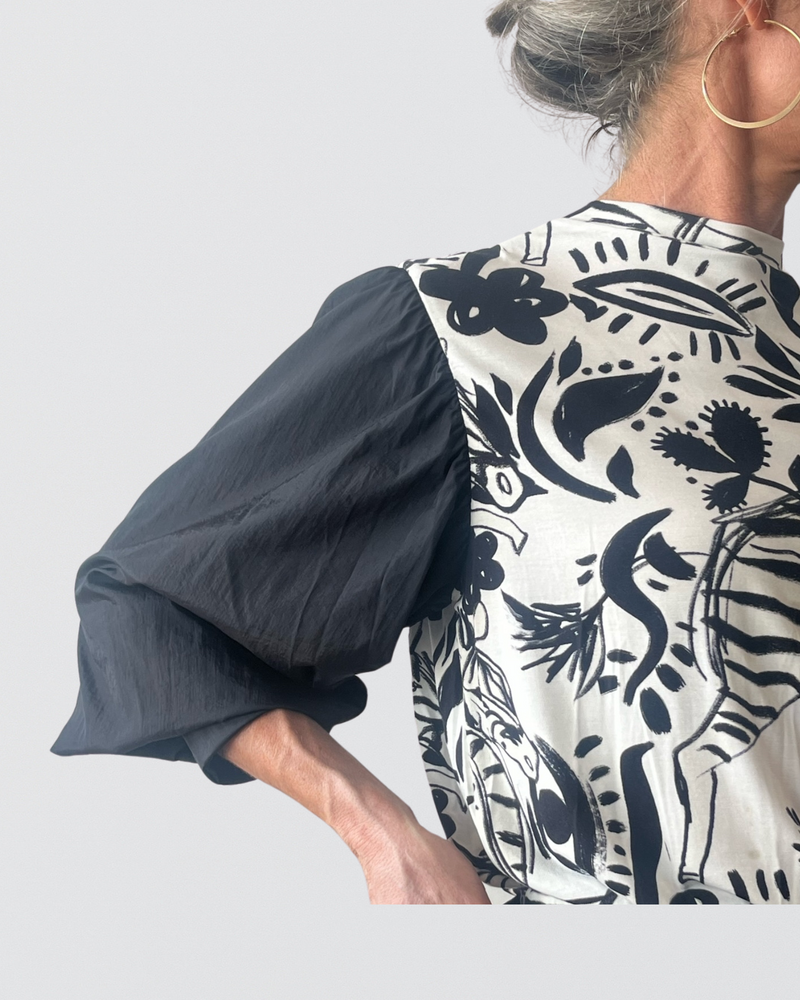 Tracey Adaptive Prism Back Top featuring dramatic black puff sleeves contrasting with a white back panel adorned with bold black floral and botanical prints, shown from a side-back angle against a light background, highlighting the garment&