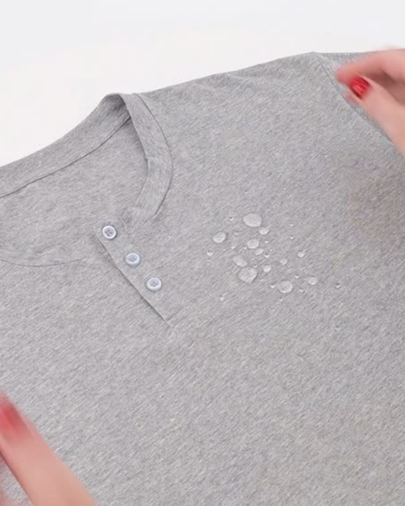 Nick A-Line Tee in heather gray featuring spill-resistant technology, with water droplets beading on the surface. Close-up view showing three-button henley neckline detail and the fabric&