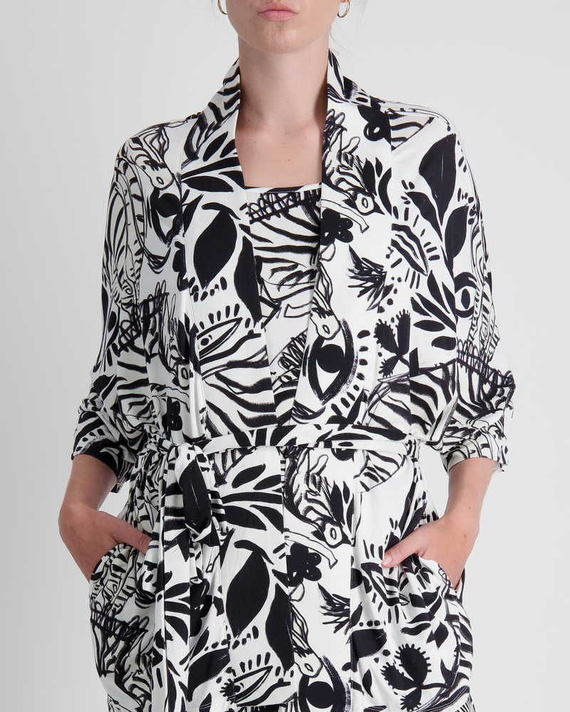 Georgie Adaptive Kimono featuring a bold black and white botanical print with abstract floral and leaf patterns. The cropped design showcases wide sleeves, front pockets, and a collared neckline, styled in a modern, seated-friendly silhouette against a light background.