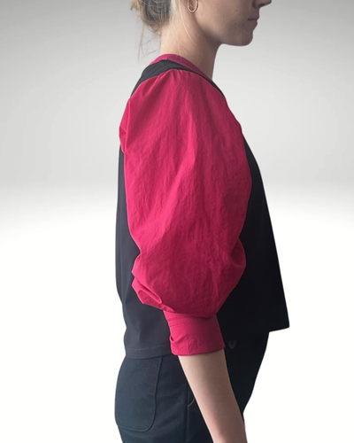 Wicky Smart-Tech Vest shown from side profile featuring black body with contrasting vibrant raspberry-colored sleeves, demonstrating its modern silhouette and adaptive design. Professional studio lighting highlights the stain-resistant fabric texture and sleek side-zip details.