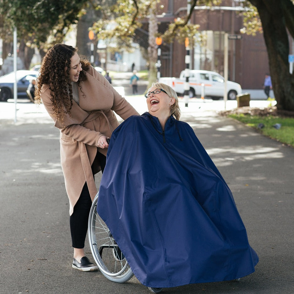 Brolly Sheets Brolly Wheelchair Rain Coat in bright yellow, designed for adaptive clothing, worn by a smiling woman outdoors.